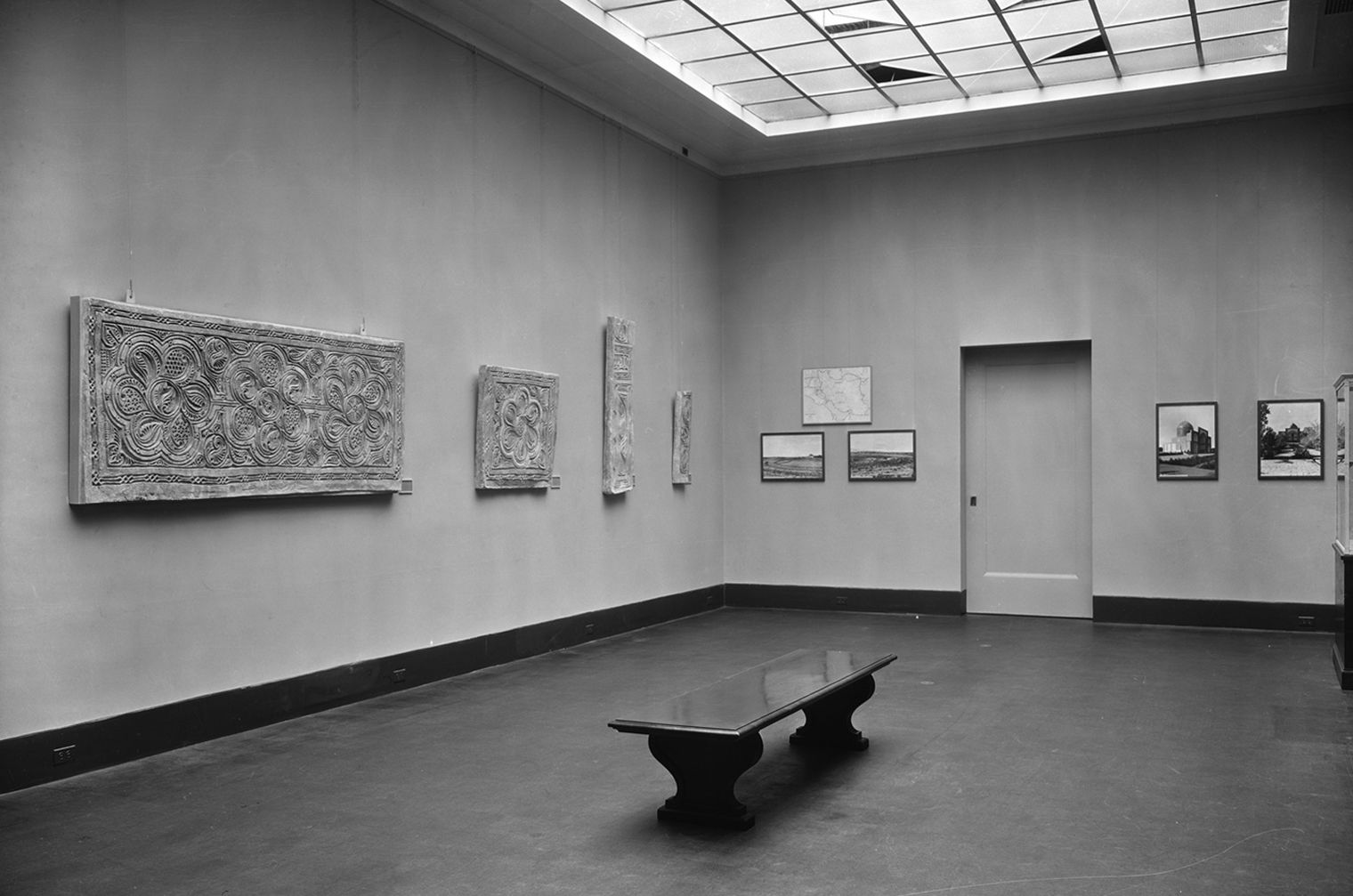 Black and white photo of a gallery from 1937 with a bench in the middle and stucco panels on the wall