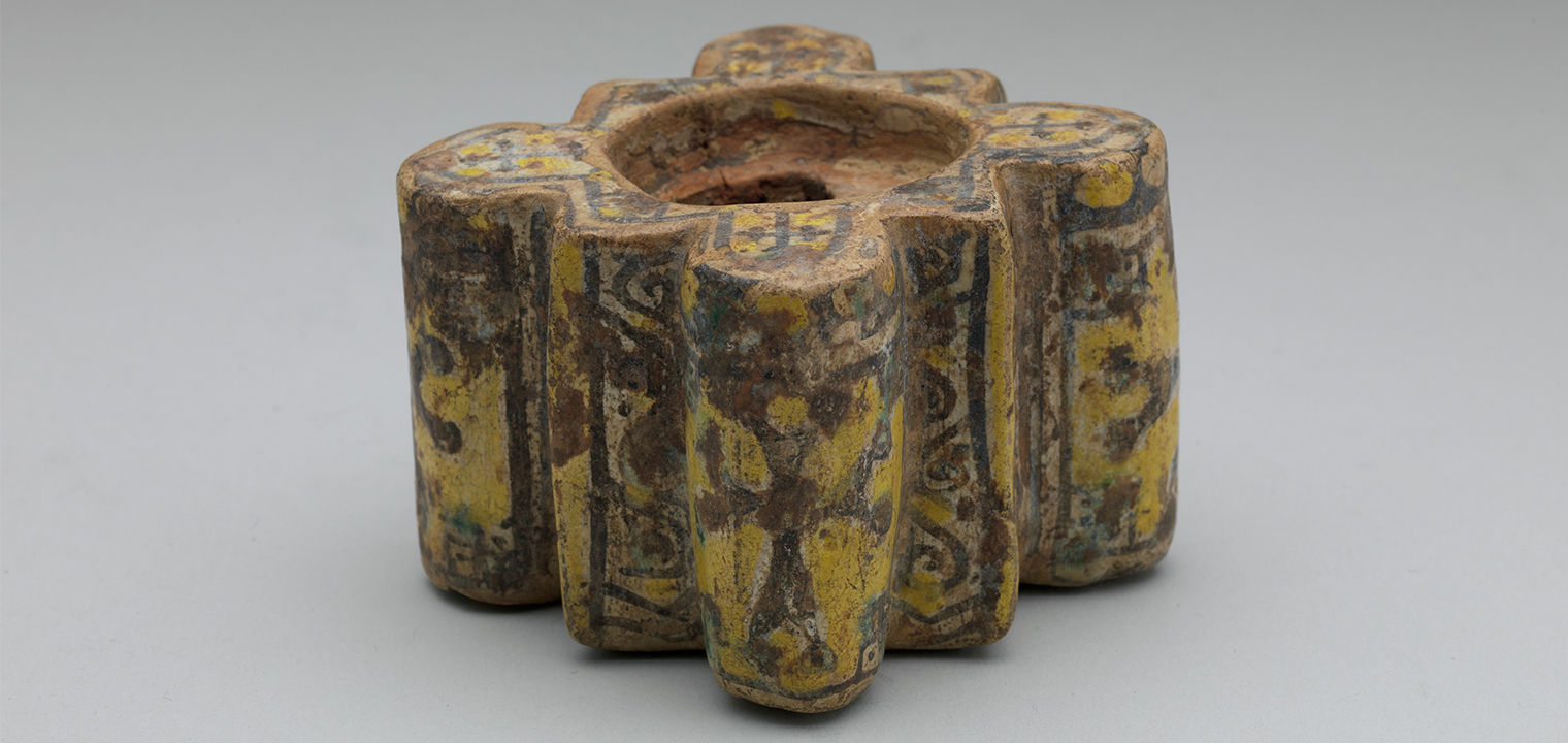an earthenware inkwell with yellow, black, and green decoration with a main decorative motif of a cross-like symbol