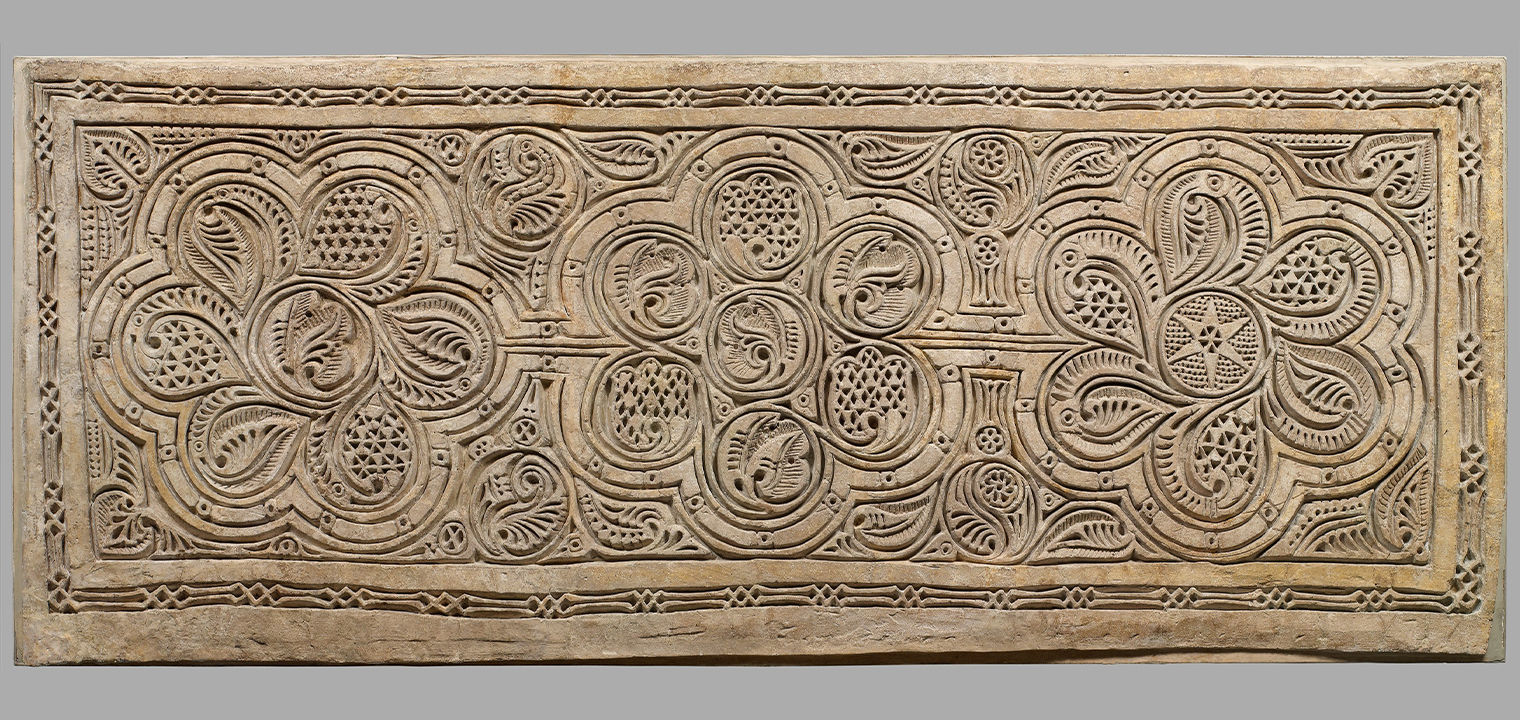 an intricately carved tan stucco panel with three main repeating floral carvings