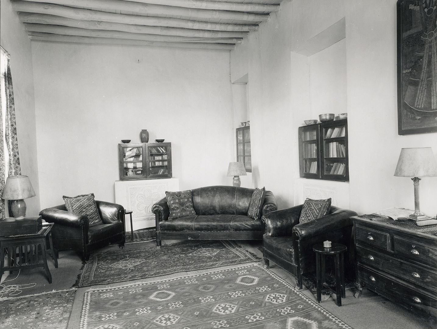 Black and white image of a living room with a couch, two arm chairs, wall cabinets, and side tables with lamps