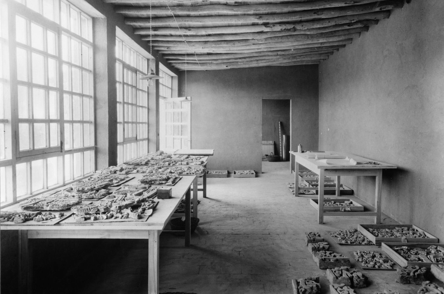 Black and white photo of interior room with scattered architectural fragments on a table on the left and on the ground on the right 