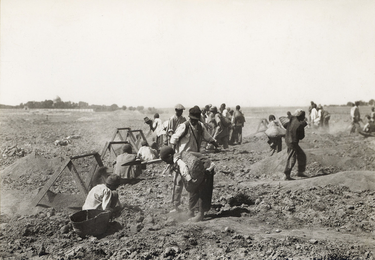 Black and white photo of boys sifting through dirt while excavating at a site in Nishapur