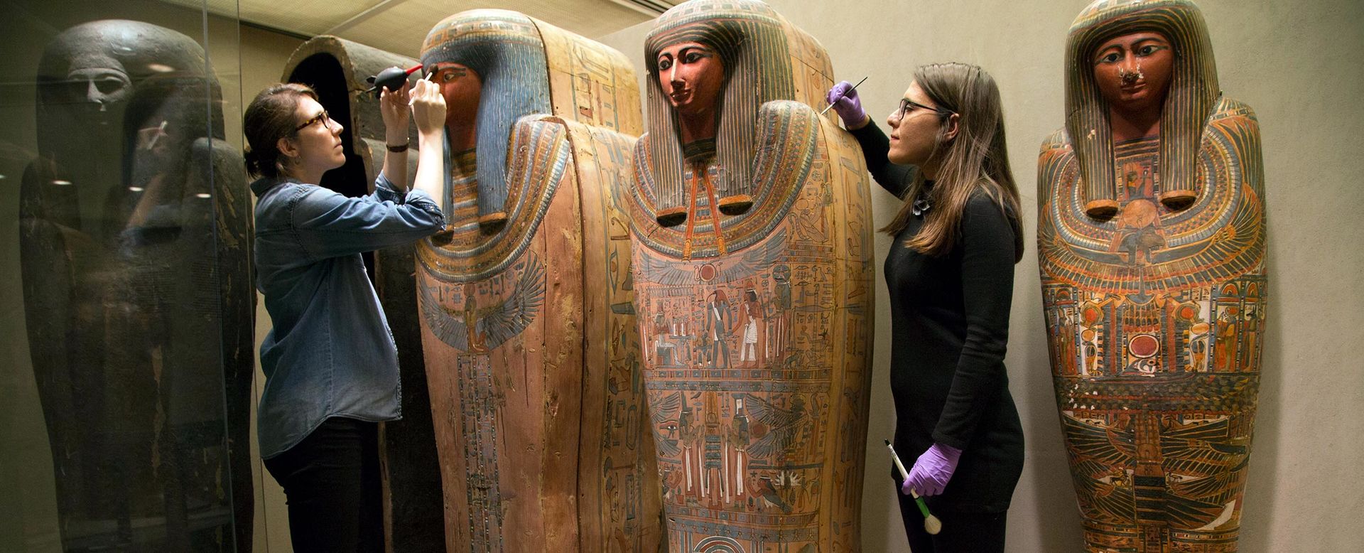 Conservation fellow and conservator use brushes to clean Egyptian coffins