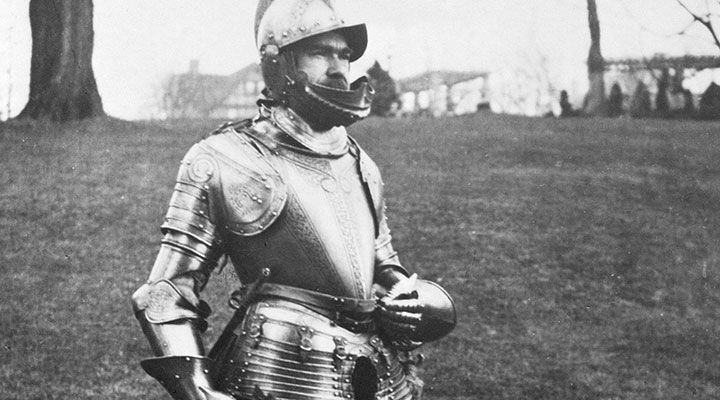 A black-and-white photograph of the late Bashford Dean wearing a suit of armor in an outdoor field.