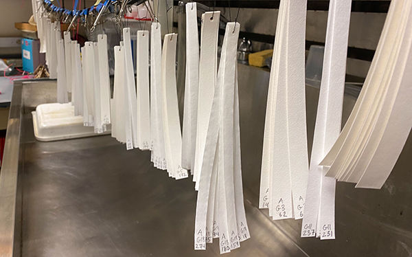 Thin strips of white paper hanging over metal sink in darkroom lab.