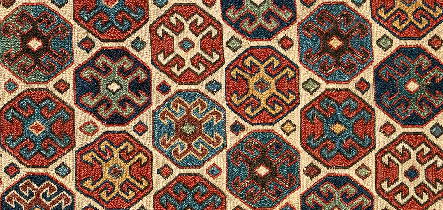 Detail from an early-20th-century, Persian saddlebag with a tan, orange, brown, and blue geometric pattern 