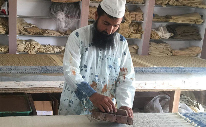 A man in a painted stained tunic creating prints for a textile