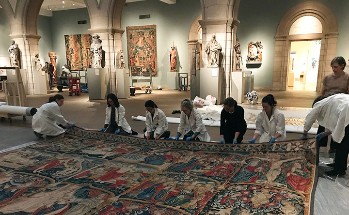 A group of textile conservators roll out a large-scale medieval tapestry in the Medieval Sculpture Hall at The Met Fifth Avenue