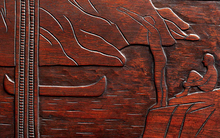 Detail from a carved chest by Robert Laurent depicting two men on a rock, one sitting and the other one about to dive into a lake