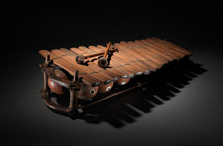 Photograph of a balafon, a xylophone-like percussion instruments made of wood against a dark background.