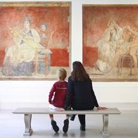A woman and young child sitting on a bench in the Roman fresco gallery looking at art