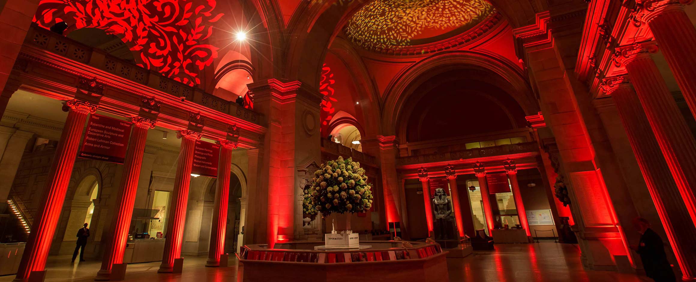A vase with green foliage stands in the center of a grand arched foyer lit up with red lights