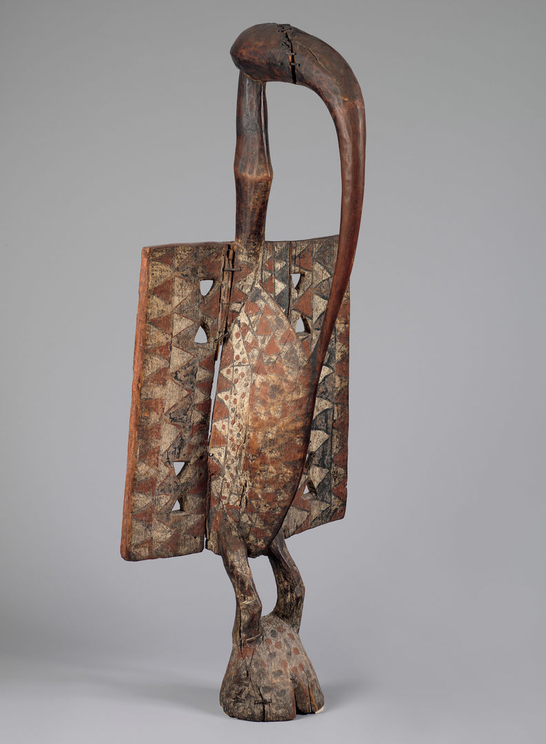 A wooden sculpture of a bird with a long neck, square wings, and a long, curved sharp beak