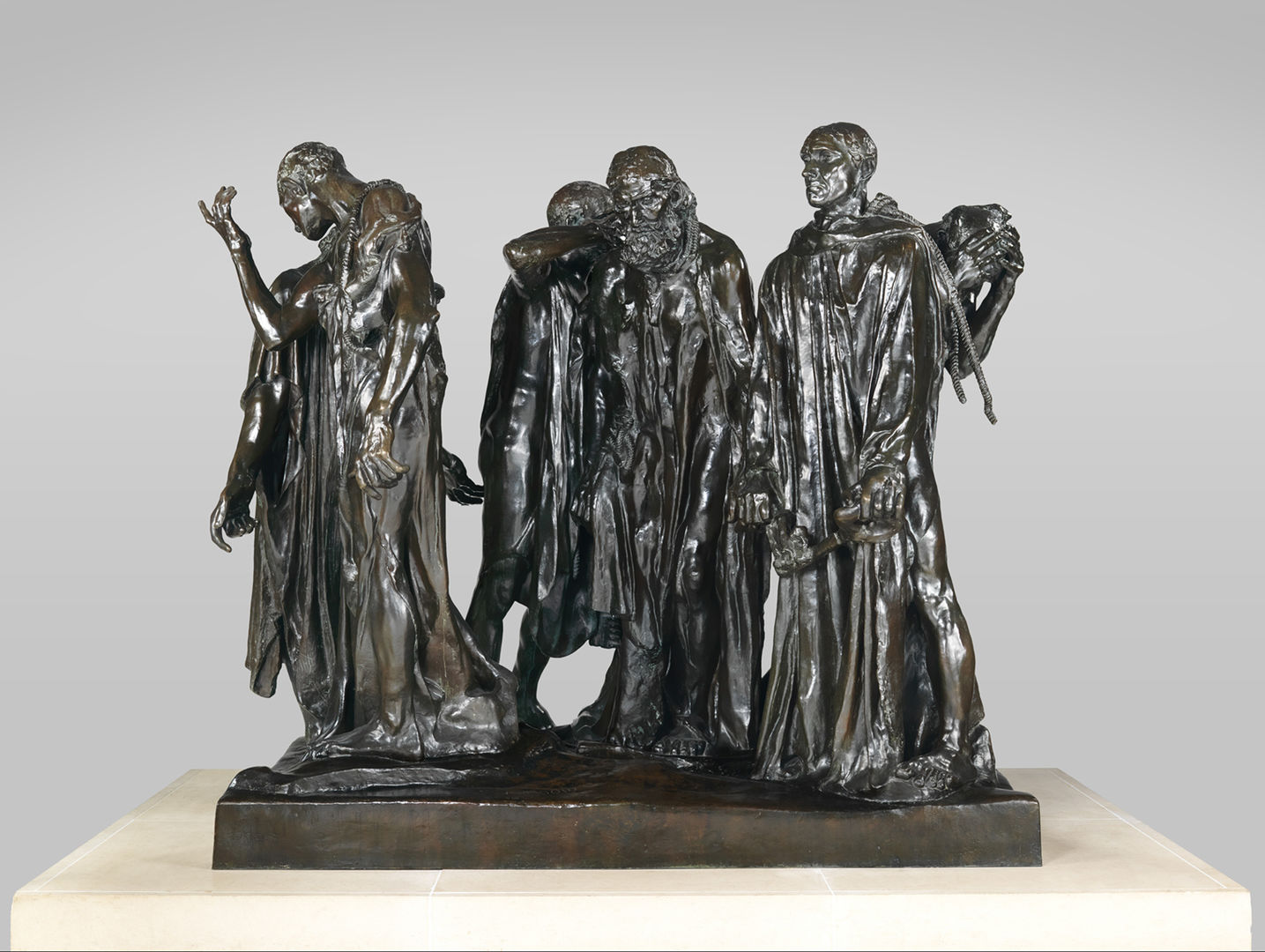 An over-life size bronze sculpture of a group of men chained together in a group, walking in a circle