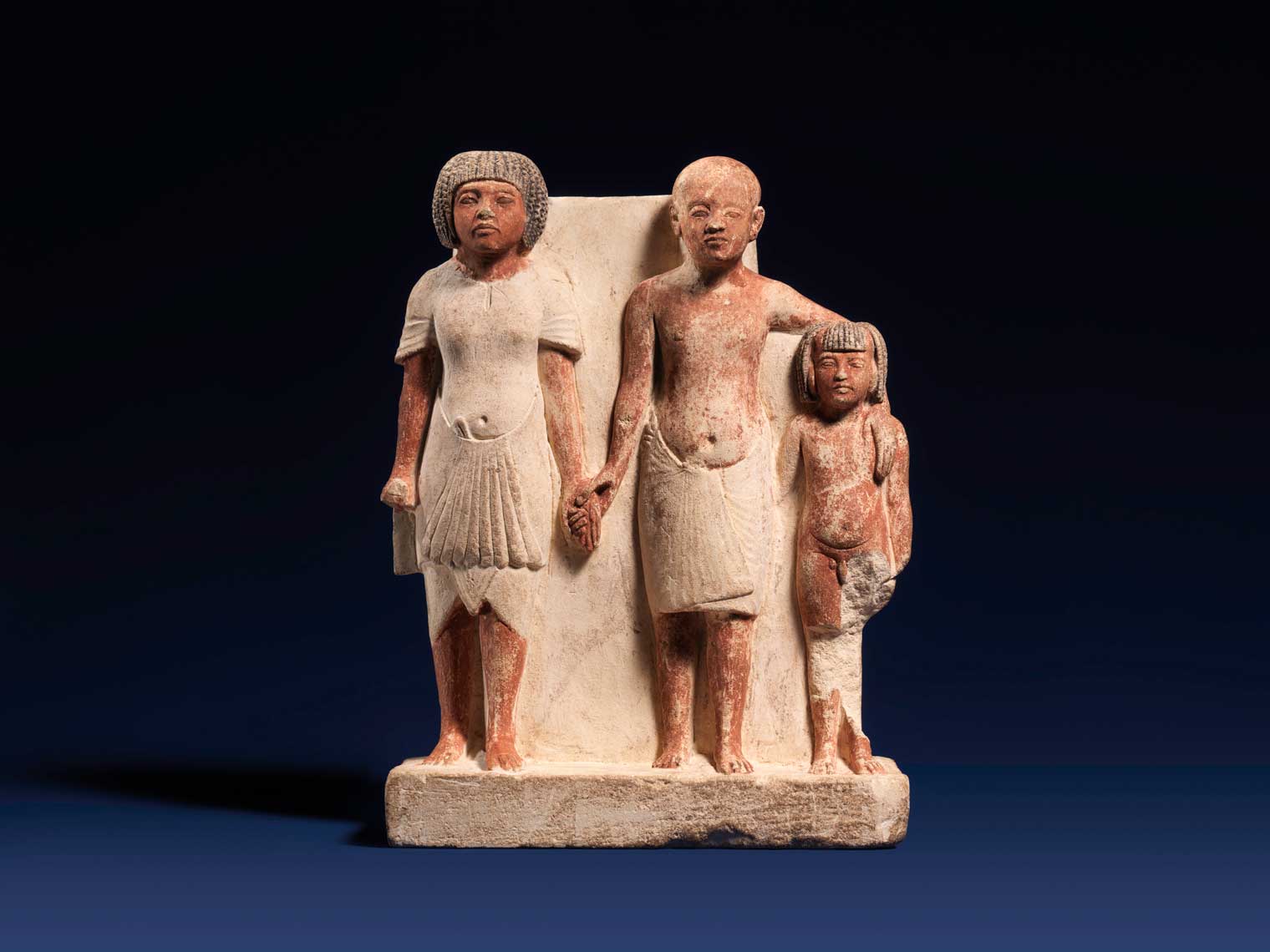 A limestone statue of two men and a boy standing side-by-side and holding hands