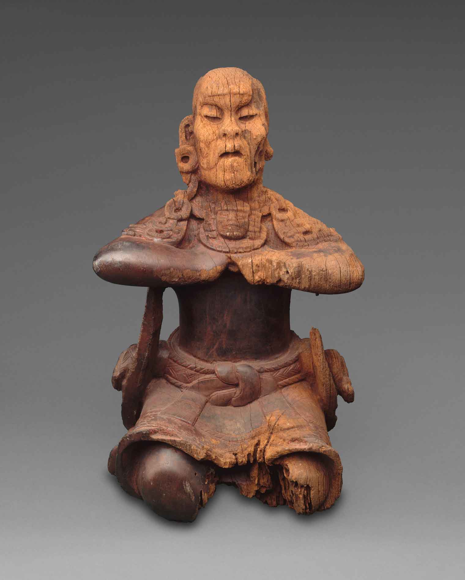 A wooden figure seated upright, with arms parallel to the ground.