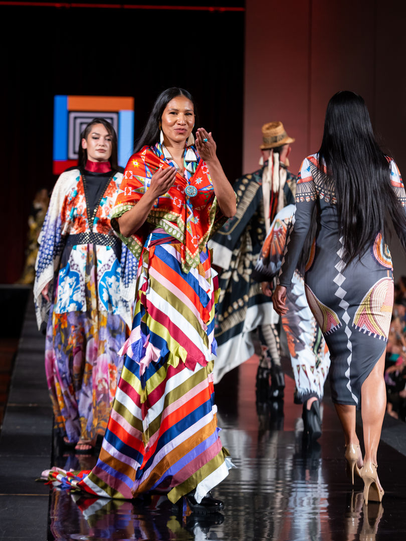Designer Jamie Okuma blows kisses to audience while walking with her models at SWAIA Indigenous Fashion Week