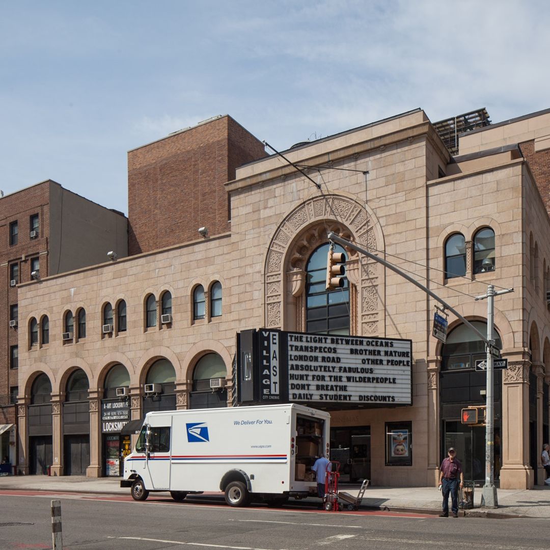 Contemporary photograph of a building with arched storefront windows including a small locksmith business and the East Village movie theater.