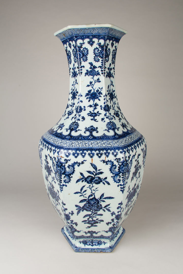 Photograph of a large Chinese vase against a grey backdrop. There are decorative patterns on the porcelain in blue and white.  
