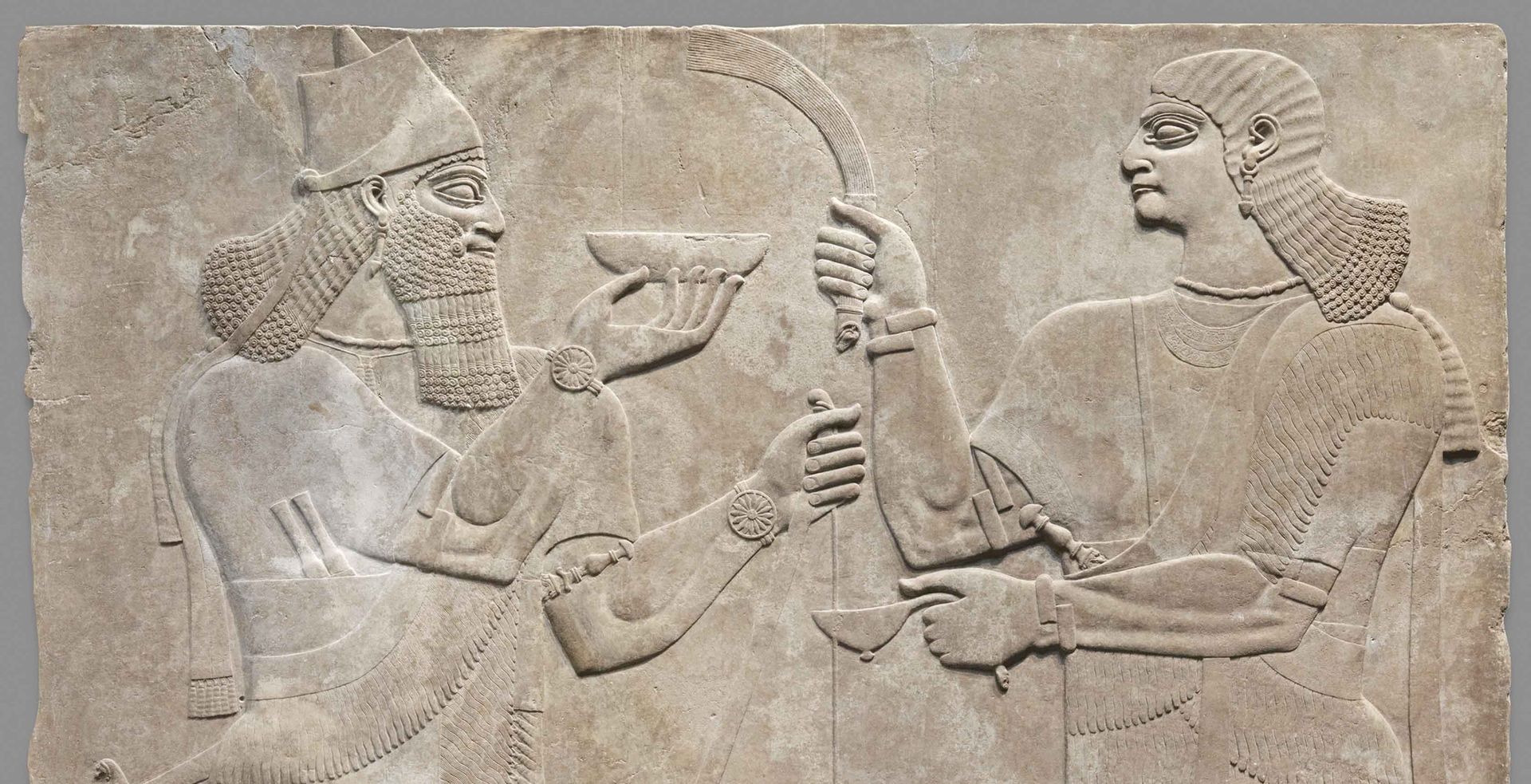Limestone Assyrian relief with a low-relief carving of two men bearing gifts