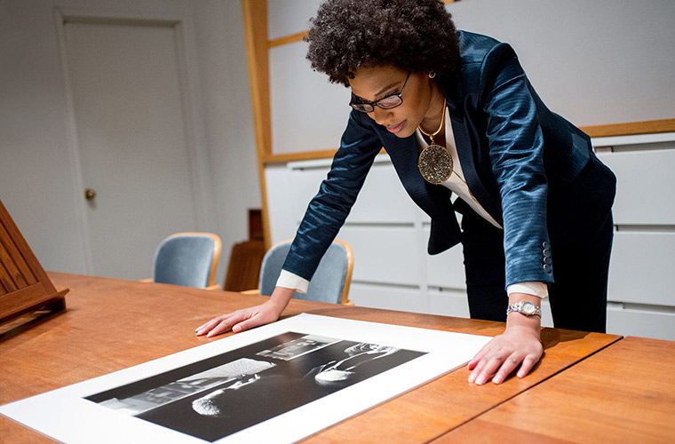 A woman leans over a table to look down at a large-scale printed photograph