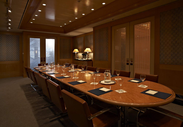A casual-elegant private dining room with blond wood paneling and fabric covered walls, leather and chrome chairs; the table is set sparingly with glasses and pitchers of water