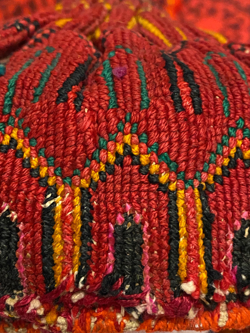 Detail image showing the embroidery on the headdress. Red is the primary color, accented by black, gold, pink, and green.