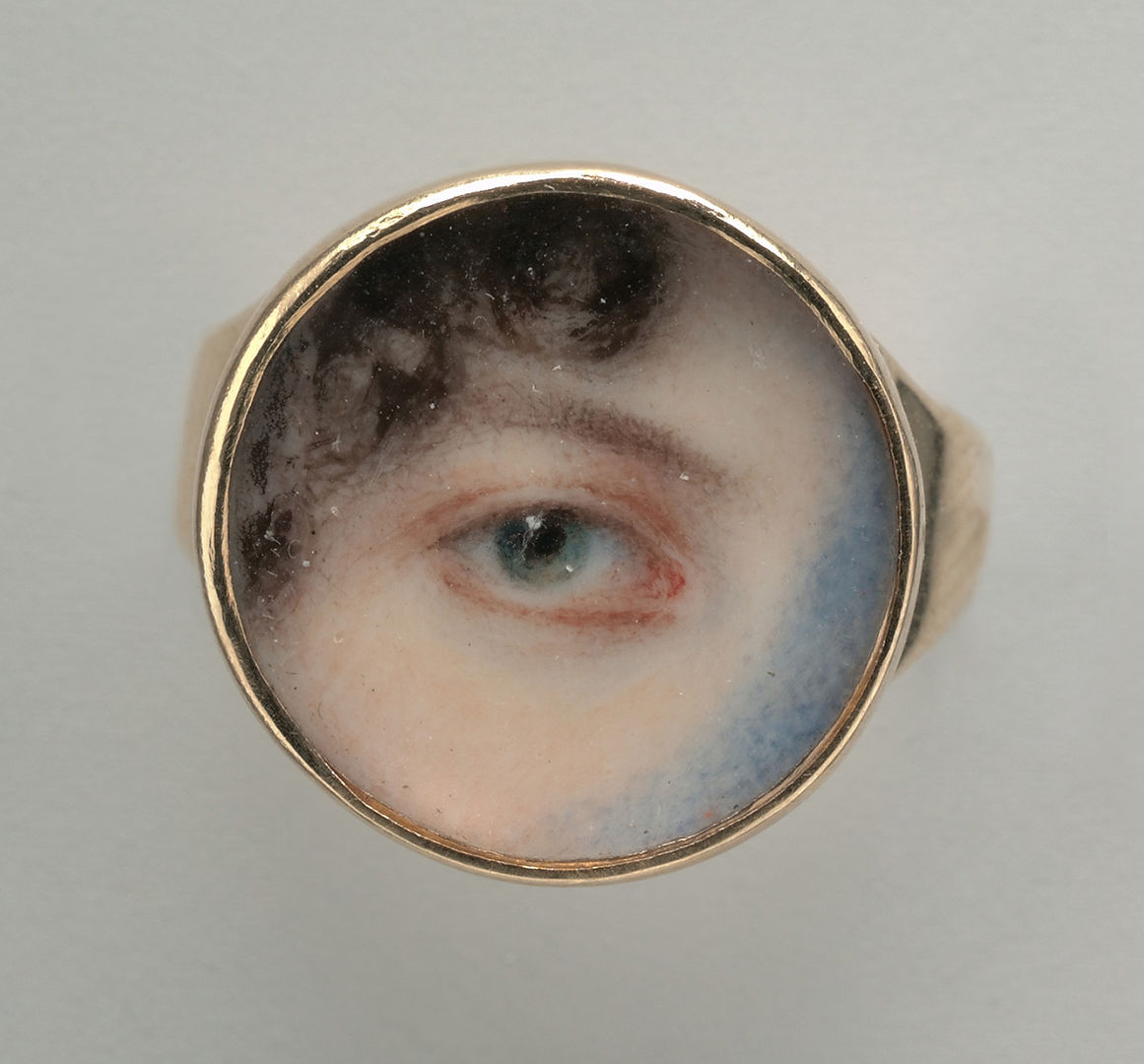 Watercolor of a 'lover's eye,' showing simply a green eye, eyebrow, and locks of brown hair around the temple in a small, circular frame.