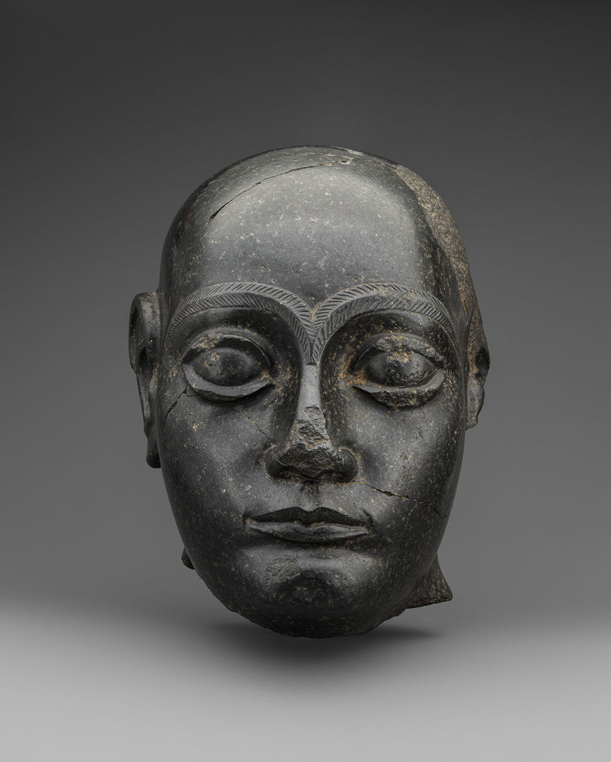 Head of Gudea in dark diorite stone. The jagged base of the neck shows where the head has been removed from the body. The left ear is also damaged.