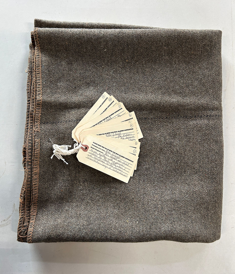 Simple, gray blanket. The tag identifies the owner as Peter Kubitschek, who elaborates that this blanket was issued to him at a Nazi concentration camp.