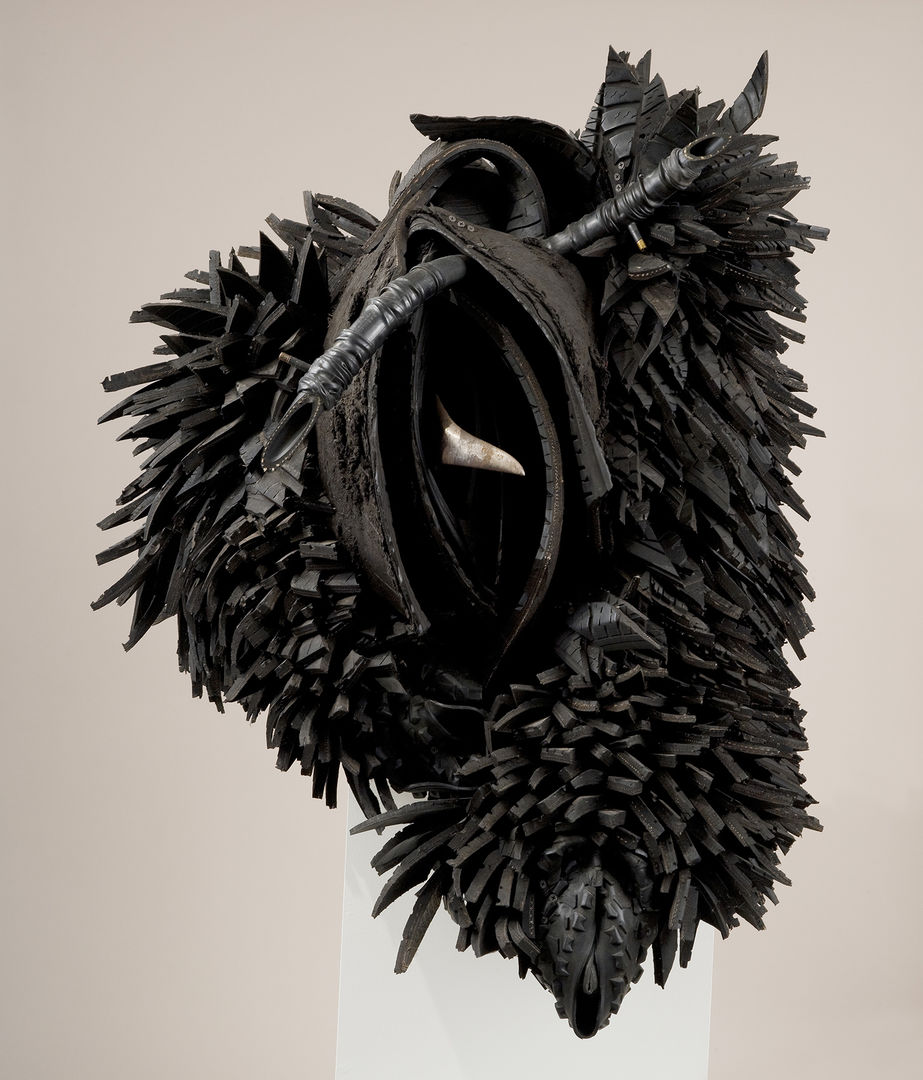 Abstract sculpture. Shredded pieces of tire with the appearance of feathers surround rows of curved rubber, resembling a vulva. A sharp piece of steel protrudes from the center.