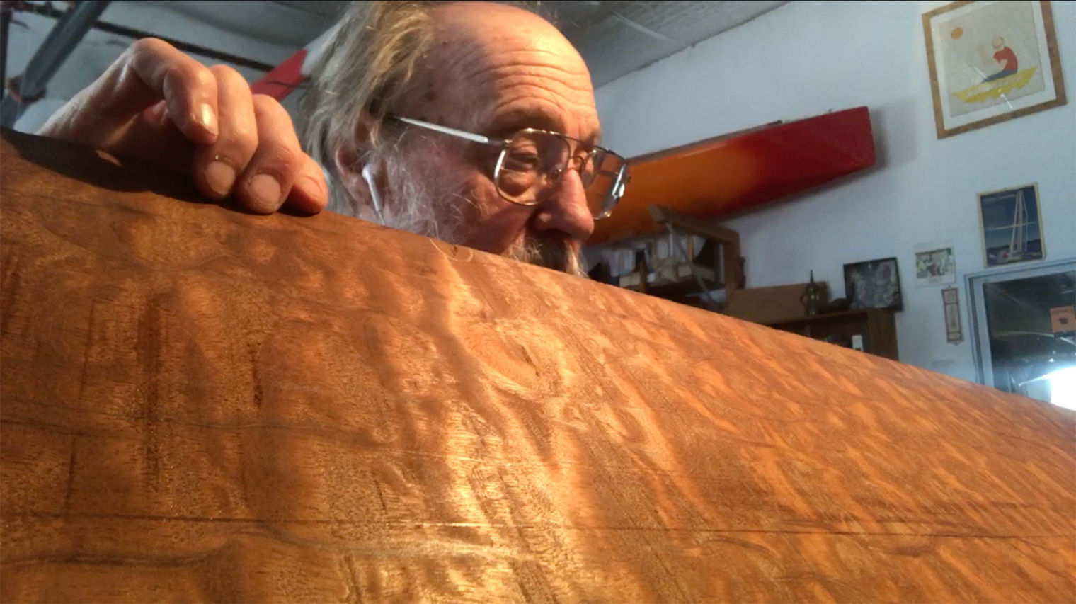 Ken Parker holds up a piece of mahogany. Light reflects of the shiny wood.