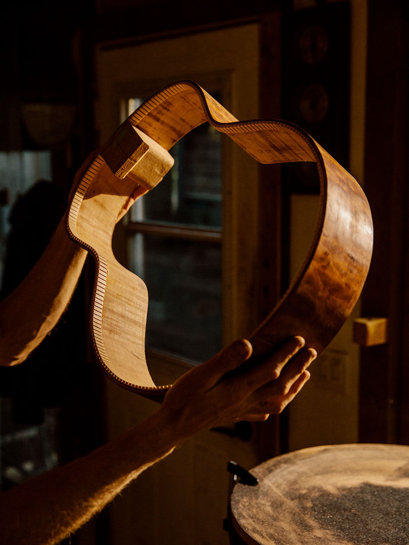 Hands holding up a piece of wood, bent in the shape of an outline of a guitar's body.